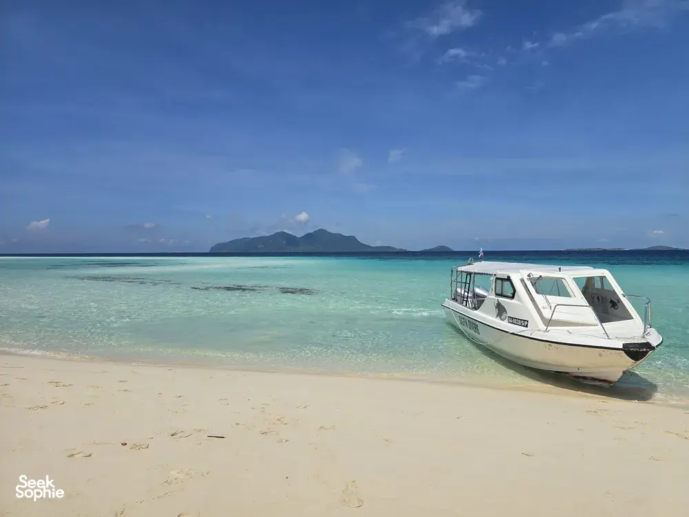 Bot laju putih berlabuh di pantai berpasir di Semporna sebelum singgah untuk snorkeling di Bohey Dulang & pulau-pulau sekitarnya bersama Bigfin Divers