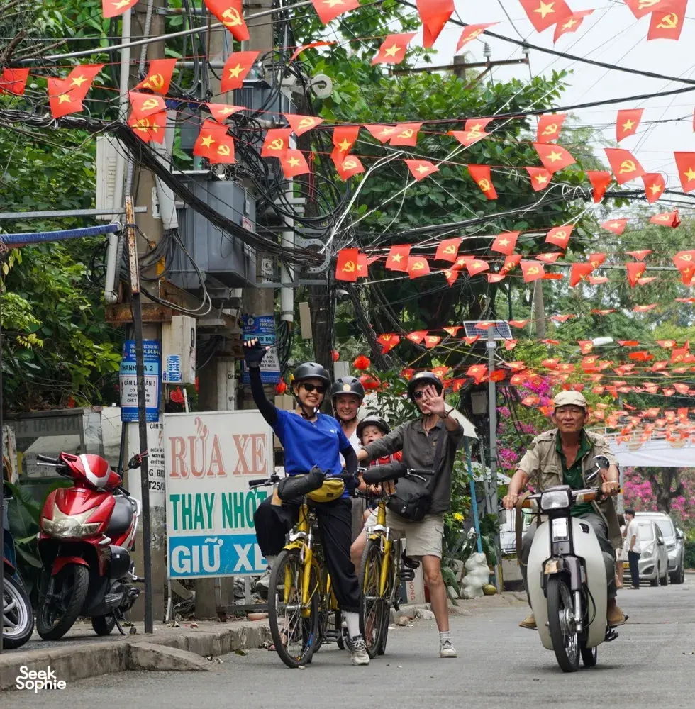 Cyclists riding along a festive street with red Vietnamese flags on Mekong Island near Ho Chi Minh City during a bike tour