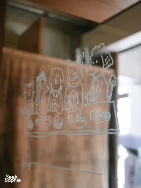 Line-drawn characters on a frosted glass panel inside a Singapore shop in Joo Chiat during a food tour