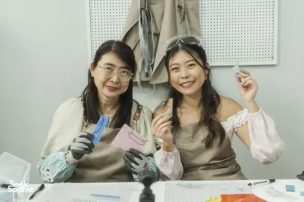 Smiling makers holding finished stained-glass suncatchers at a craft table, posing with their work during workshops in Singapore