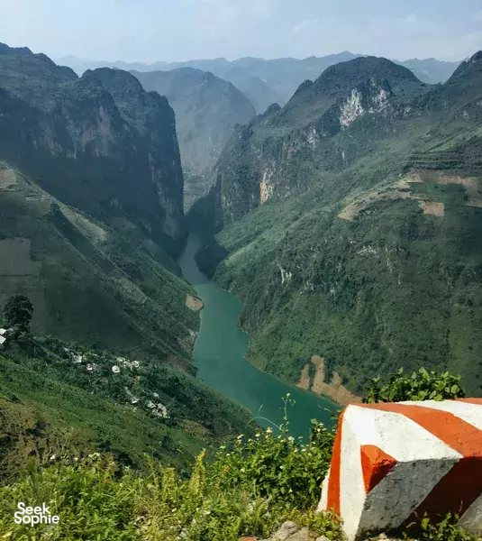 Scenic lookout over a deep mountain gorge and green river on the Ha Giang Loop, with a viewpoint railing in the foreground