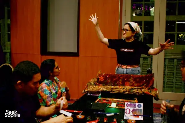 Story-driven tabletop roleplaying game in Singapore with a host gesturing to players around a board game table — team building Singapore