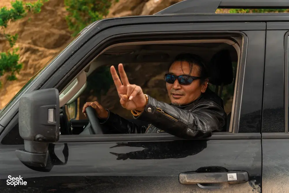 Tibetan guide in a tour car window giving a peace sign on the road to Shangri-La during the 6-day loop