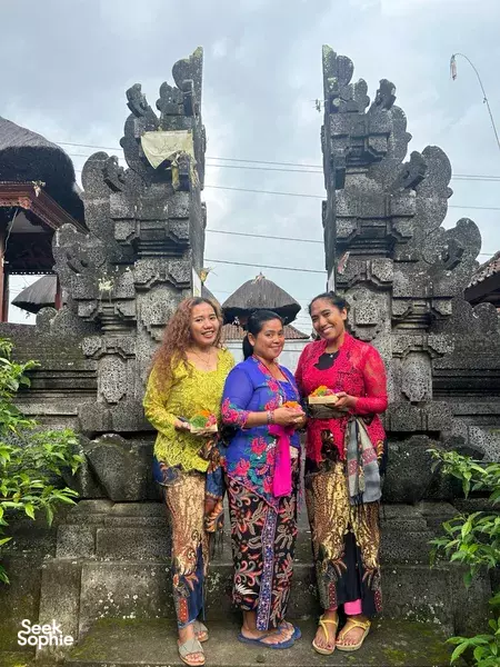 Women in traditional Balinese dress pose before a stone temple gate as part of the Tri Hita Karana visit in Bali