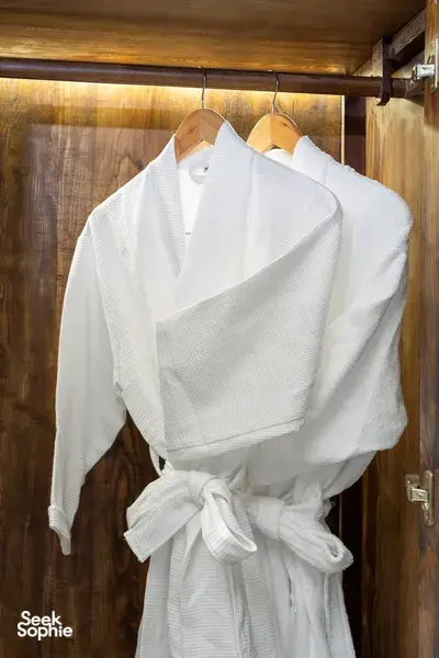 White bathrobe hanging on coat hooks inside a wooden wardrobe in Cat Ba Ocean Cruises’ cabin on the 3D2N Cat Ba cruise