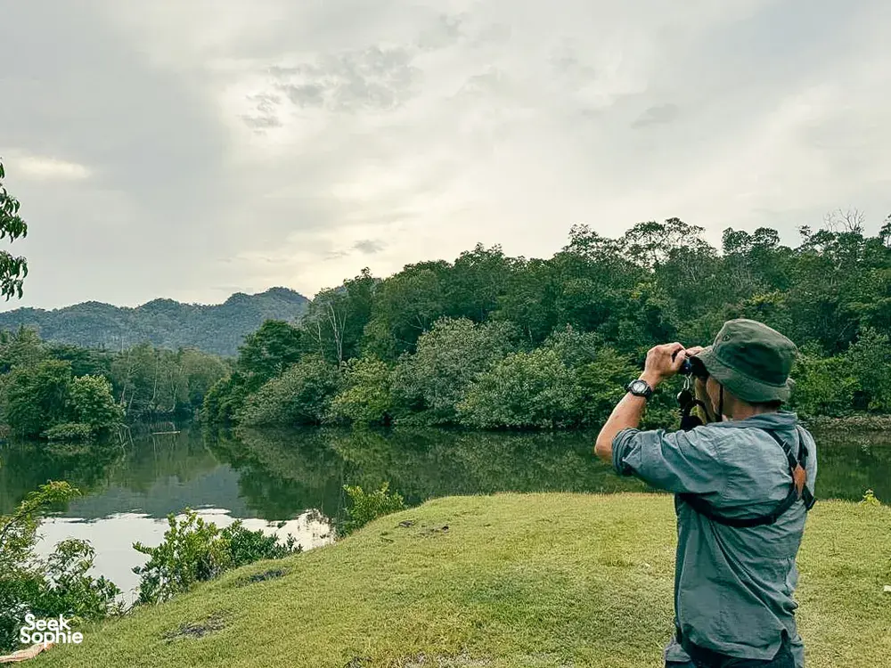 Nature lover photographing over a calm lake bordered by green hills and forest in Langkawi during a guided birdwatching stop