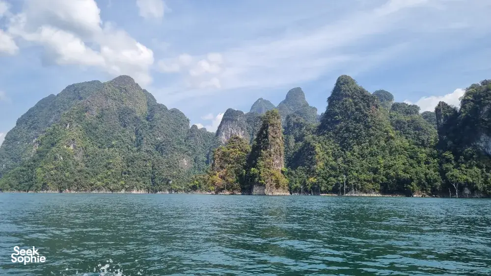 Green rainforest covering limestone towers across the lake, captured from a boat on Khao Sok National Park