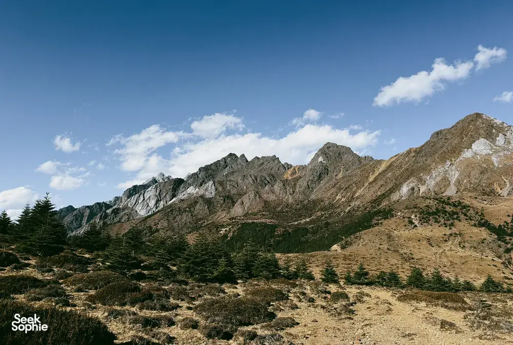 Jade Dragon Snow Mountain ridgeline near Lijiang under a blue sky, with rocky slopes and scattered evergreen trees