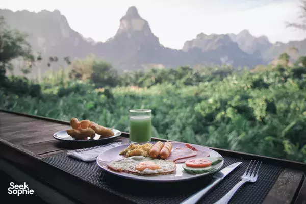 Outdoor breakfast set on a wooden table at Anurak Lodge—eggs, toast and fruit—during a stay in Khao Sok National Park