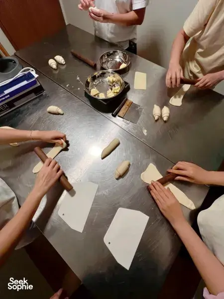 Hands portioning shio pan dough at a The Daily Staples workshop in Singapore, with floury pieces, trays and rolling tools on the bench