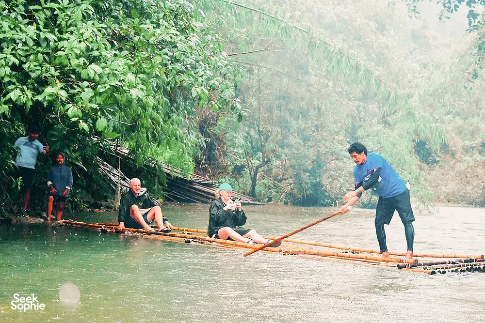 Travellers sit on a bamboo raft guided by a paddler on a misty river, during the Half-Day Cycling & Rafting in Khao Lak