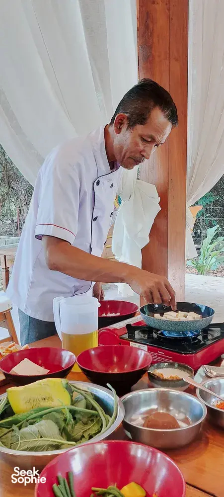 Chef Michael cooks at the counter, with pans and bowls of vegan ingredients ready for a Manggarai cooking lesson in Labuan Bajo