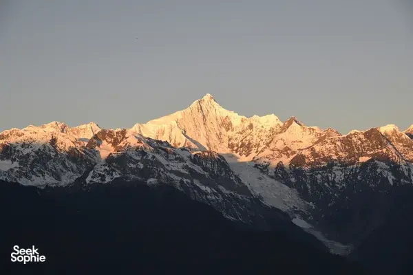 Snowy Meili Snow Mountain summit lit by early sunrise rays above dark ridgelines on a 2D2N adventure from Shangri-La