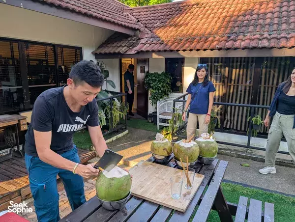 People preparing ingredients at a table with halved coconuts and drinks in the courtyard of a seaside farm in Singapore