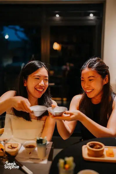 朋友们在新加坡一间温馨的小店里一起品尝清酒,笑着举起小酒杯——摄于 SakeMama