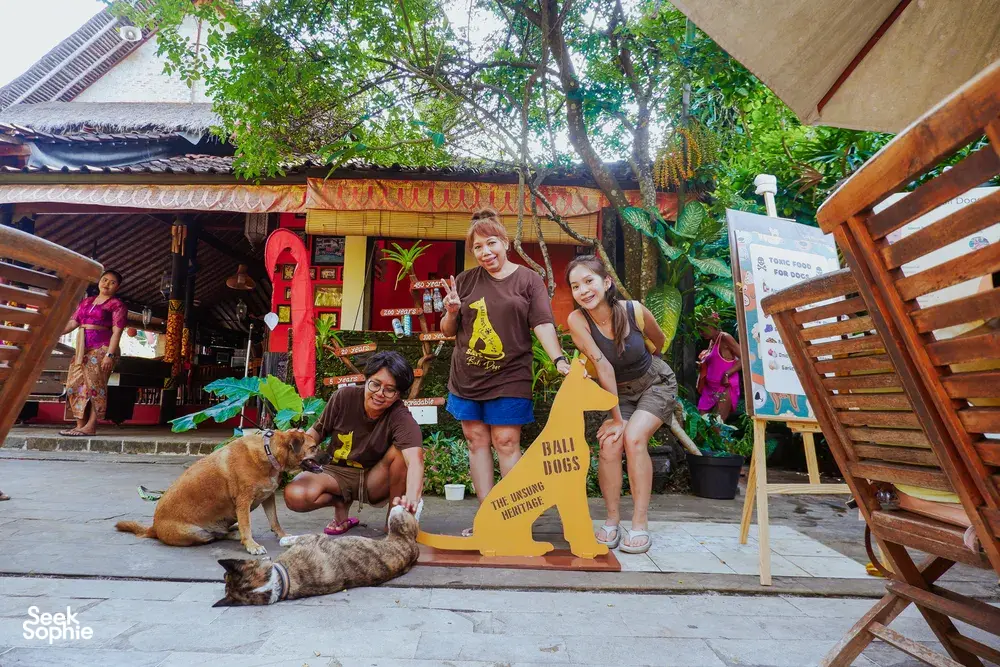Visitors and staff pose with dogs beside a “BALI DOGS” sign at a Bali conservation centre run by Bali Conservation Adventures
