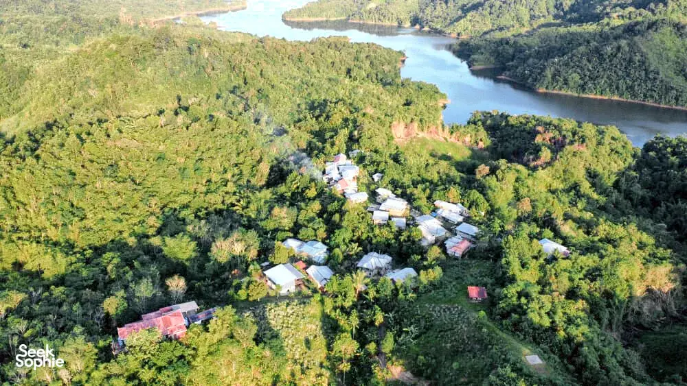 Aerial view of clustered homes, forest, and a winding river at a Bidayuh ancestral land regenerative homestead near Kuching