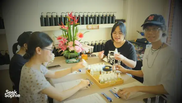 People at a Singapore candle-making table measuring scent oils, with rows of fragrance products behind them in a perfume workshop