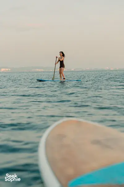 Woman stand-up paddleboarding on open water from a catamaran near Kota Kinabalu in the late evening light