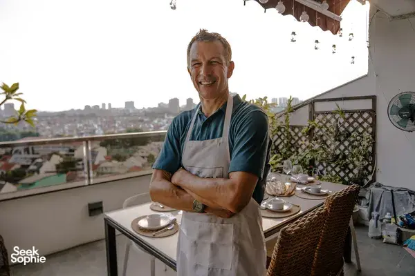 Eric from French Cooking Lab smiles on a Singapore balcony during a laid-out sunset drinks session with city skyline behind