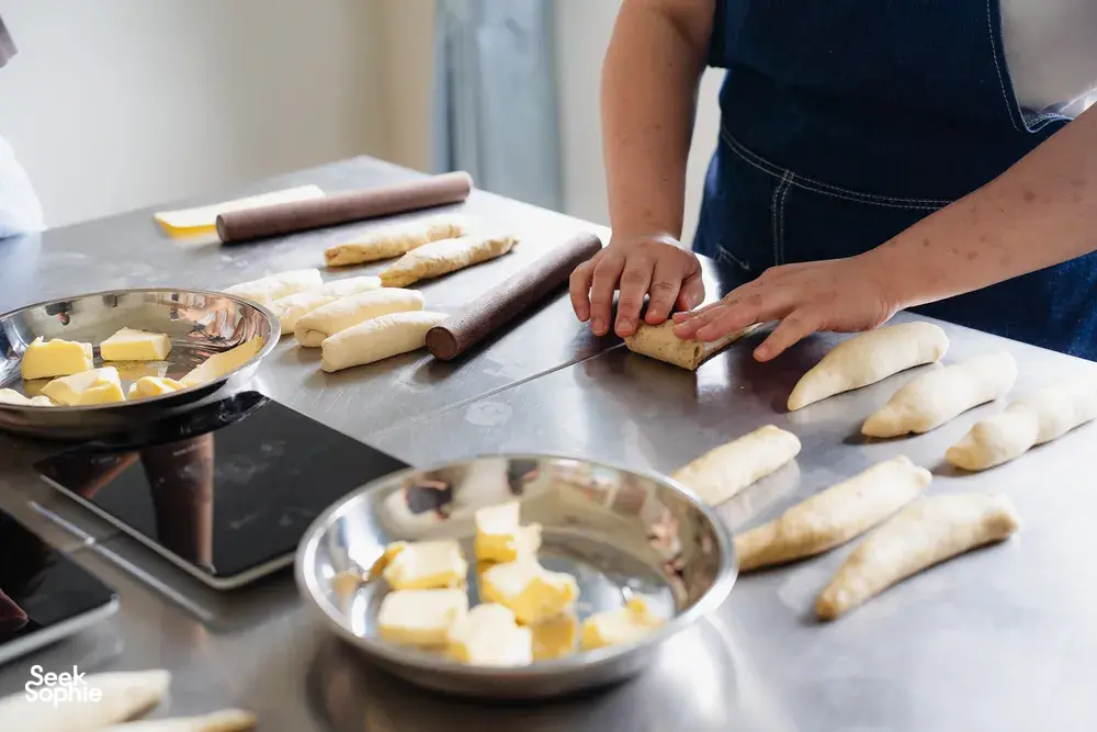 Hands shaping shio pan dough on a metal bench beside a bowl of butter at a bread-making session—workshops in Singapore