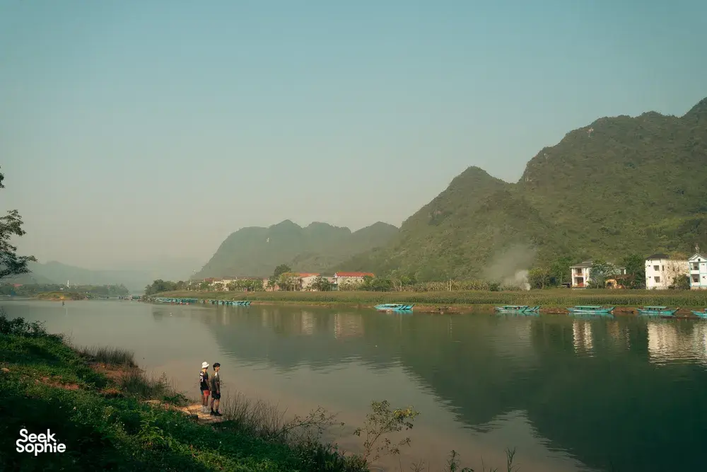 Slow riverside walk in Phong Nha as travellers head along a calm river bordered by lush banks and tall green hills