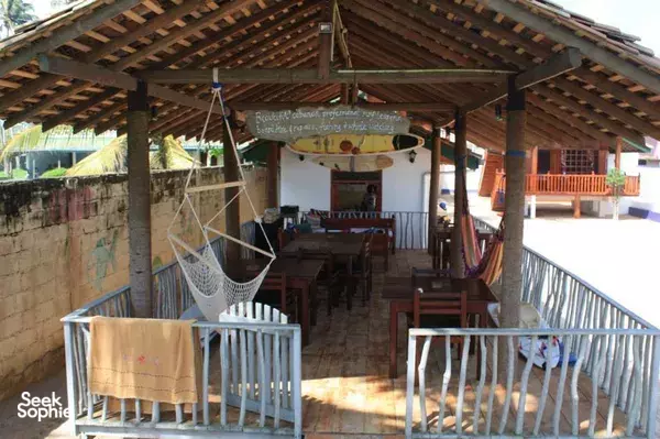 Open-air dining veranda with a wooden roof, tables and chairs, a hammock, and hanging laundry at The Green Rooms, Weligama