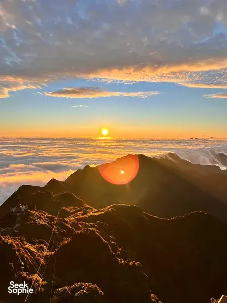 Golden sunrise from a mountain ridge above Sapa, with winding paths and ridgeline haze glowing at Mt Fansipan