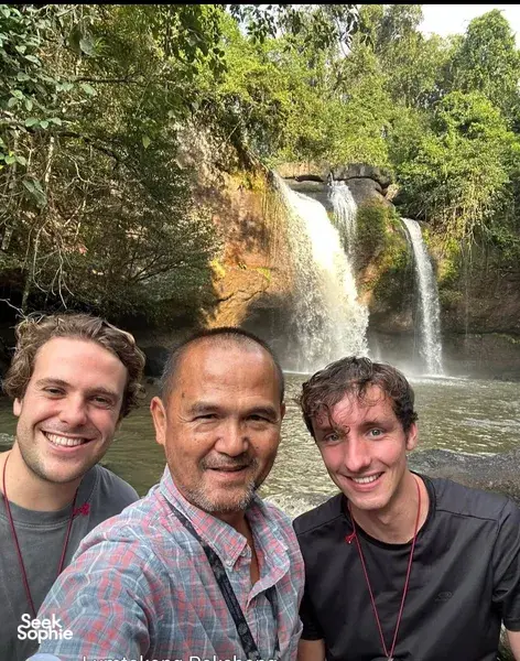 Travellers pose with a local guide beside a waterfall in Khao Yai National Park during a wildlife trek hike