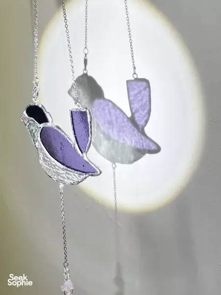Purple and silver stained glass bird suncatcher silhouettes hanging in sunlit light, made for workshops in Singapore