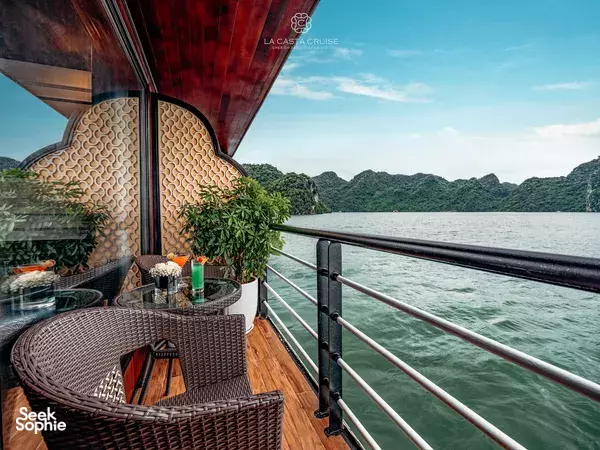 La Casta Cruise private balcony with a wicker dining set and patterned wall details beyond the rail, facing waters in Lan Ha Bay