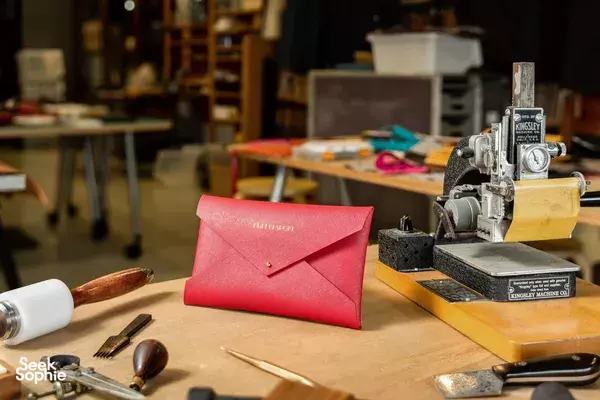 Red mailer cardholder on a workbench beside a leather sewing machine at Kult Bespoke in Singapore, ideal for workshops in Singapore