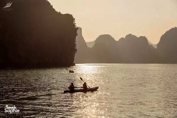 Passengers in a small boat at sunset on Lan Ha Bay, Halong Bay, with limestone cliffs silhouetted in the distance