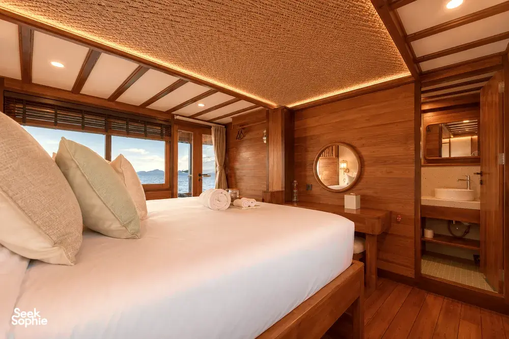 Komodo Island phinisi cabin bedroom with a large double bed, warm wooden walls and a round mirror, Travass Life 3D2N stay