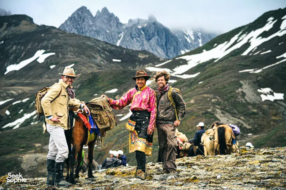 Backpackers meeting a mule caravan on a snowy, rocky mountain trail in Shangri-La’s high-altitude valleys