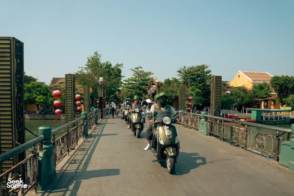 Deretan skuter Vespa melaju di sepanjang dermaga tepi sungai di Hoi An bersama Hoi An Backroad Tours, menuju serunya naik perahu keranjang