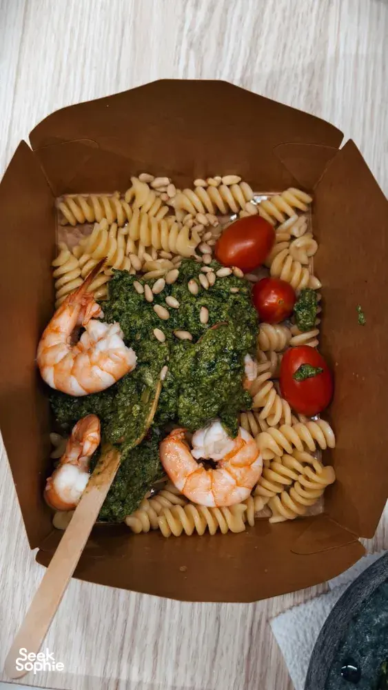 Cardboard deli box of pesto pasta lunch with basil, cherry tomatoes and shrimp on a table in Singapore workshops in Singapore