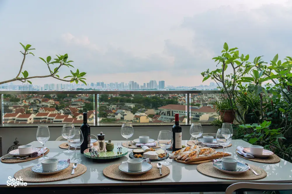 Balcony table set with wine, glasses and plates beside potted plants, with Singapore skyline views—private dining Singapore