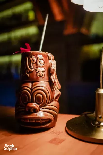 Carved tiki-style drink cup with straw on a wooden table during a Foodie Tours in Da Nang tasting stop