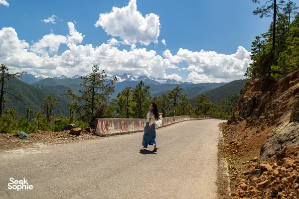 Walker on a mountain road near Shangri-La, with Meili Snow Mountain’s snowy peaks across the valley under blue sky