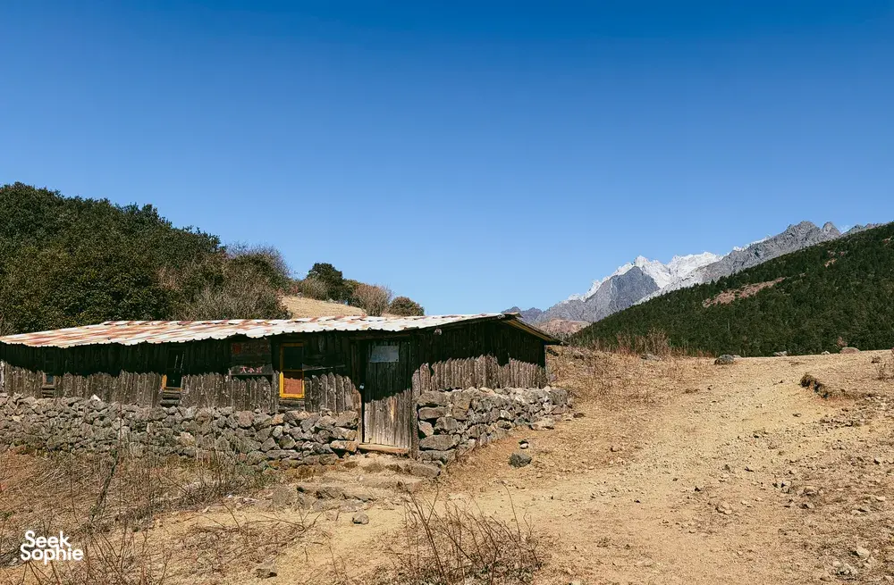 Wooden mountain camp hut overlooking distant peaks during a guided hike to Jade Dragon Snow Mountain from Lijiang