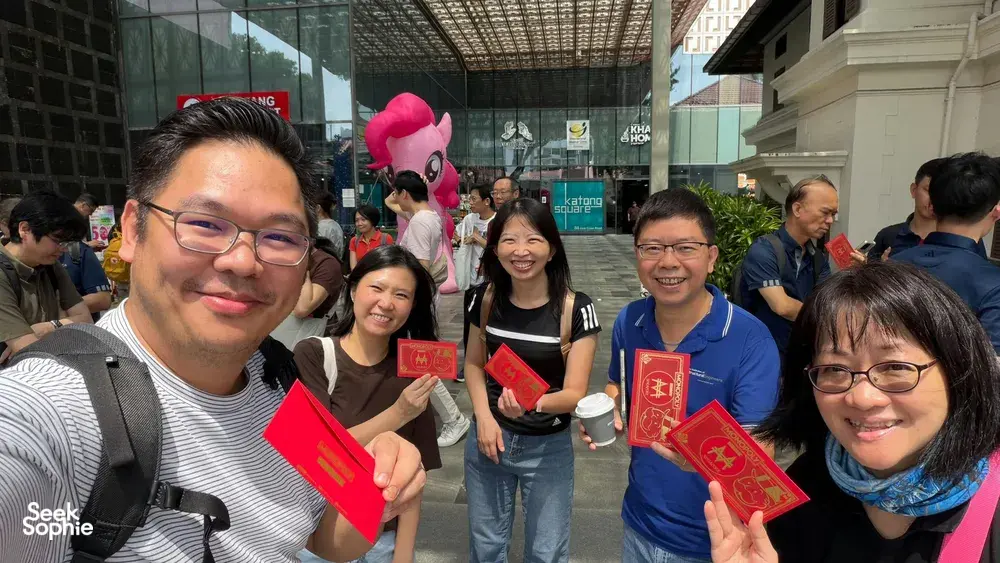 Team members smiling and holding Monopoly-style red cards during a real-life game in Katong-Joo Chiat, Singapore for team building Singapore