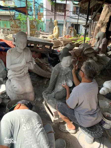 Saigon sculpture workshop where artisans work on white clay statues, with plaster figures and tools arranged along a sunlit aisle