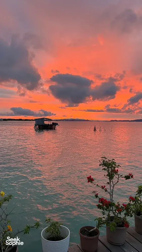 Matahari terbenam dari dek banglo air di Semporna, dengan pemandangan laut dan rumah terapung, serta penginapan Bigfin Divers di atas teluk