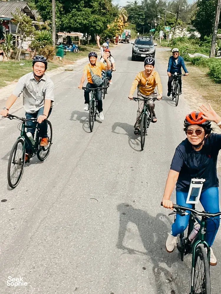 Cyclists ride along a quiet rural road through green gardens during a Half-Day Cycling & Rafting experience in Khao Lak