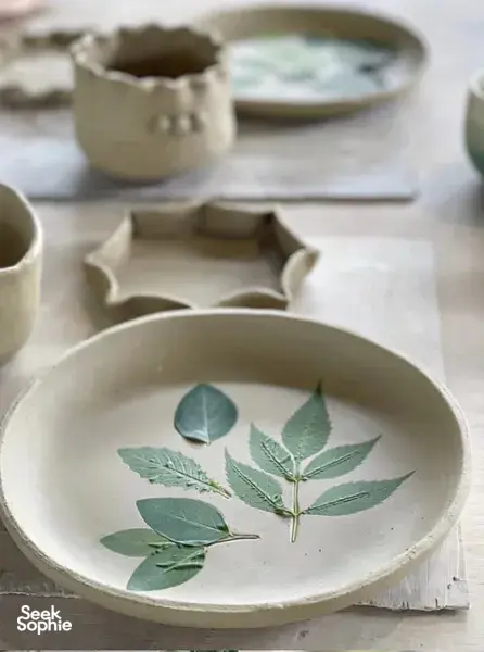 Hand-painted ceramic bowl with a botanical leaf design at Ilham Ceramic Studio in Langkawi, with other pieces in soft focus.