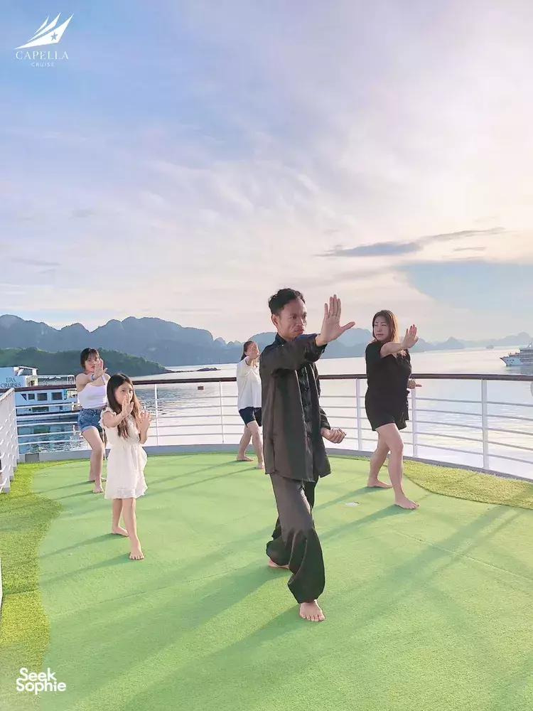 Barefoot stretching on the cruise deck yoga mat with calm sea and distant karsts behind on a Lyra Cruise Collection cruise in Halong Bay