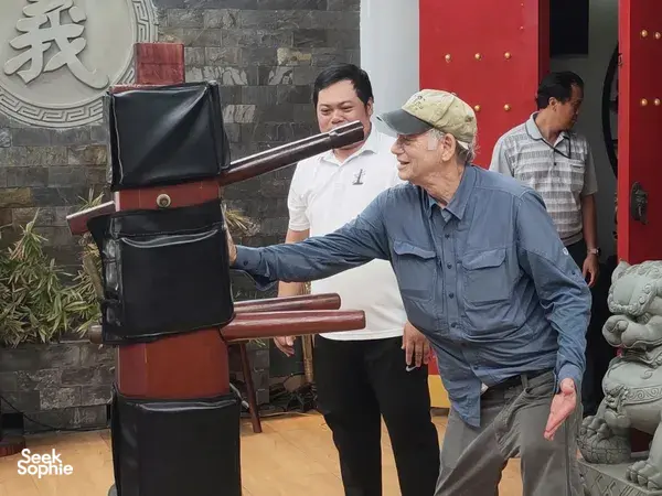 Guide demonstrating lion dance equipment in a courtyard in Ho Chi Minh City, with guests watching near a decorative stone guardian