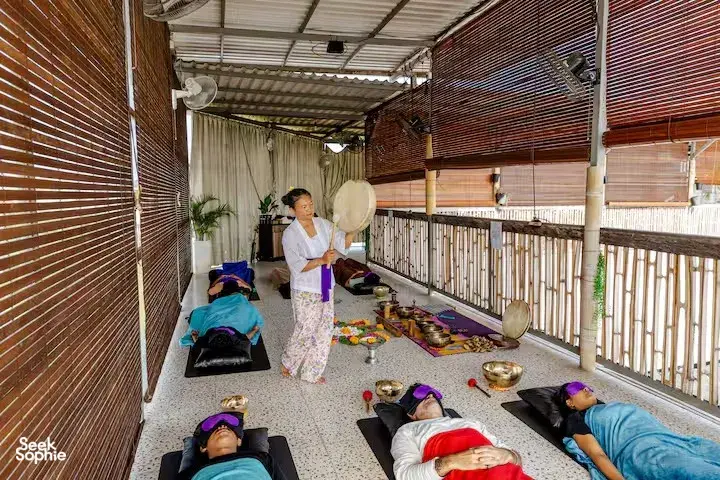 Lying guests in a guided sound healing session at ADDA Yoga in Canggu, with bronze singing bowls along the rooftop