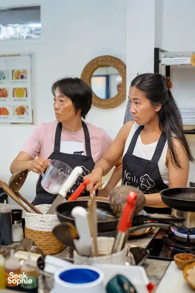 Two cooks in aprons measure and prepare ingredients at a Gili T cooking class in Lombok kitchen, focused and attentive